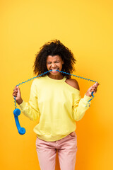 angry african american woman biting cable of vintage telephone on yellow