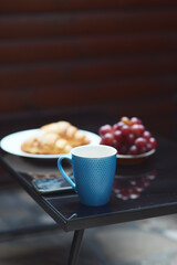 Morning begins after coffee. A cup of coffee, croissants on a plate, red grapes and smartphone on the black table. Selective focus. Copy space. Vertical shot