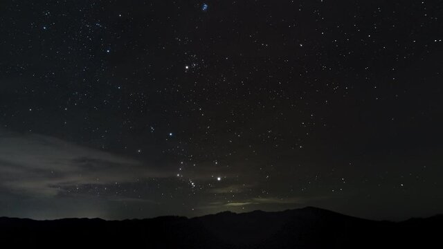 Timelapse of moving stars and clouds over the mountains in night sky. 4K