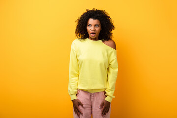 shocked african american woman with open mouth looking at camera on yellow