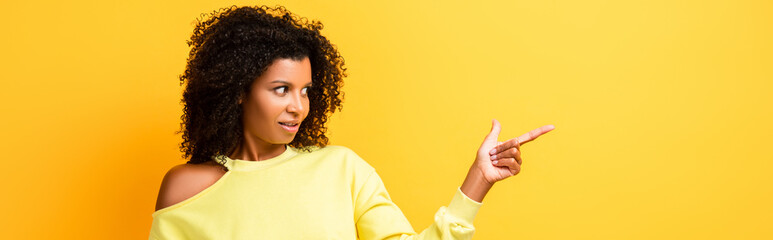 surprised african american woman pointing with finger on yellow, banner