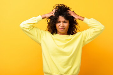 african american woman with closed eyes fixing curly hair on yellow