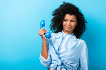 dissatisfied african american woman holding retro telephone on blue