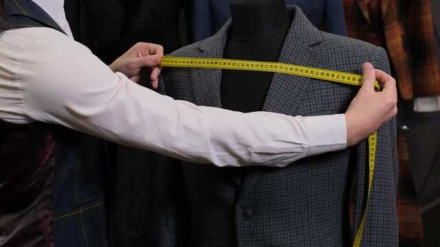 The tailor measures the suit on dummy or mannequin with a measuring tape close-up