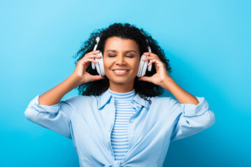happy african american woman listening music in headphones on blue
