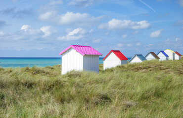 Fototapeta na wymiar Beach huts in the dunes. Picturesque colorful wooden beach cabins at Gouville-sur-Mer, Cotentin, Normandy, France