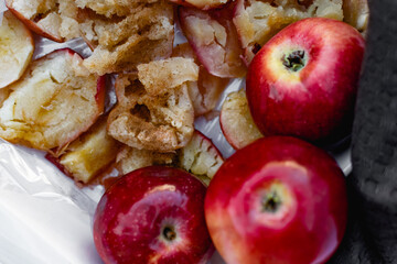 Collapsed soft baked apples in a white ceramic square shape on a special package. A white tablecloth is laid carelessly on the table, next to a dark napkin and ripe juicy red apples