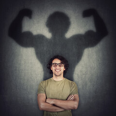 Confident young man shadows transforms into a muscular person on the wall as metaphor for inner strength. Motivated guy imagine flexing big biceps as super power. People self defense concept.