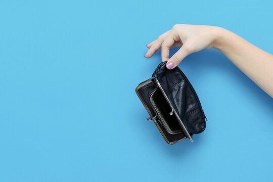 Female hand holding empty wallet on blue background with copy space. Lack of money. Poverty and bankruptcy concept