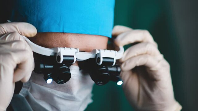 male neurosurgeon in glasses with magnifying macro lenses with illumination operates on a patient.