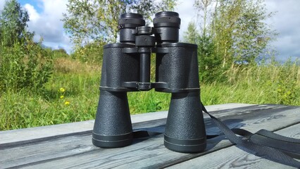 old black binoculars on a wooden surface against a background of green grass