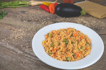 Natural rice with vegetables, risotto on the vintage wooden table decorated with fresh colorful vegetables.