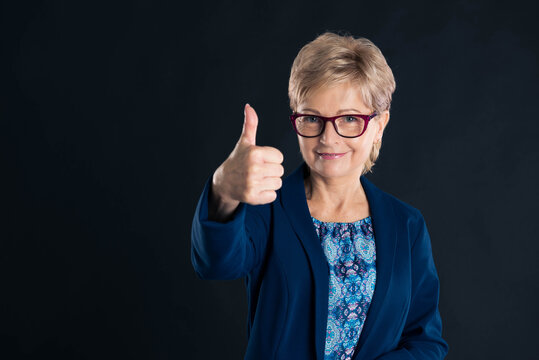 Beautiful older secretary showing thumbs up and smiling  to the camera