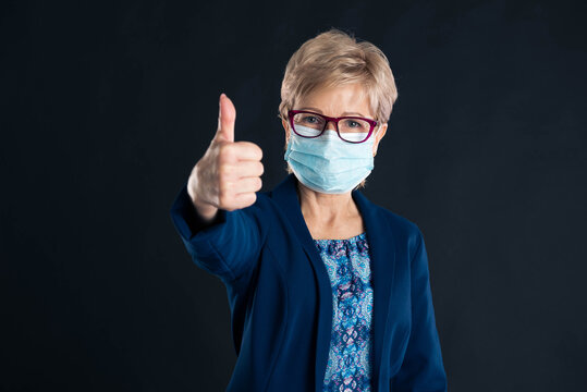 Older woman wearing a mask and showing thumbs up