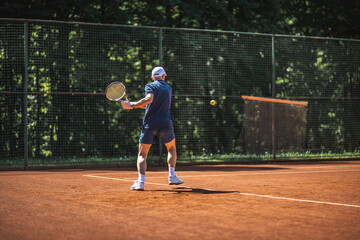 Active senior Caucasian man in sportswear playing tennis, hits a backhand groundstroke