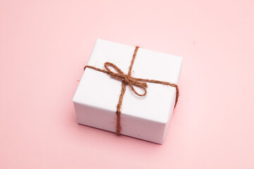 Gift box wrapped in white paper on pastel pink background