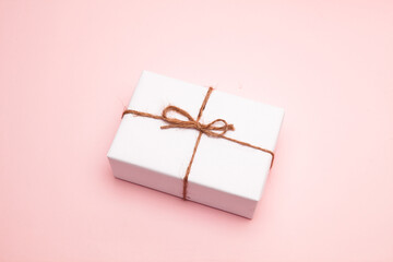 Gift box wrapped in white paper on pastel pink background