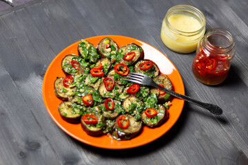 Aubergine salad with herbs and spices on red plate on black wooden background