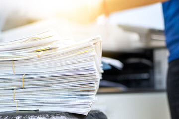 The papers stacked waiting to be copied with a copier machine.