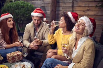Fototapeta premium drunk group of young adults celebrating new year's eve with santa clause hats on their heads and glasses of white wine in their hands, having fun outdoor in the backyard