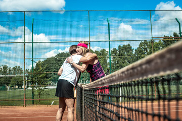Two active senior Caucasian women in sportswear playing tennis, hugging after the match
