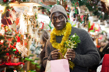 Cheerful African American looking for New Year decorations in traditional street market.