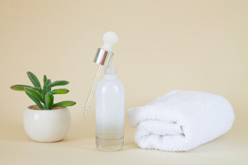 Obraz na płótnie Canvas Cosmetic clear glass open serum bottle next to plant and towel