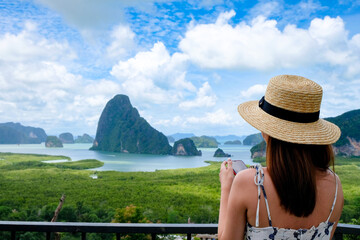 Happy Young Traveler Woman Raised Arm take a photo To Sky Enjoying A Beautiful Of Nature Samed Nang Chee on mountain landscape view point at jame bond island seascape at Antaman sea in thailand. 