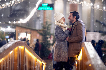 A young couple in love standing on the beautiful bridge at christmas festival on a snowy weather in...