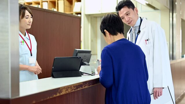 病院の受付で高齢患者の介助をする医師と受付事務員