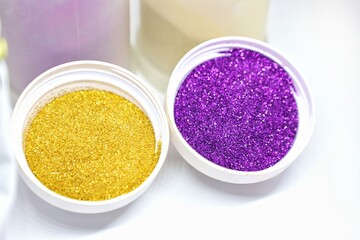 Two white bowl full of golden and purple color powder glitters isolated on whiyte background