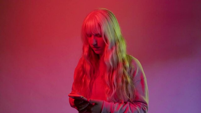 Studio shot young blonde caucasian woman on red background using smartphone isolated enjoying trends addicted to social media