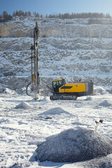 Mobile drilling machine in the snow-covered stone quarry in a winter sunny day.