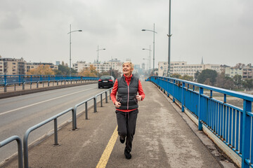 Active senior woman running through the city during the day.