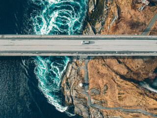 An aerial view on a hydrogen vehicle crossing a bridge with powerful waves visible in the water below.