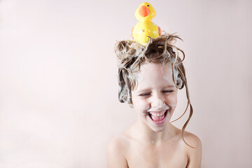 a little girl washes her hair with shampoo and plays with a toy duckling on her head