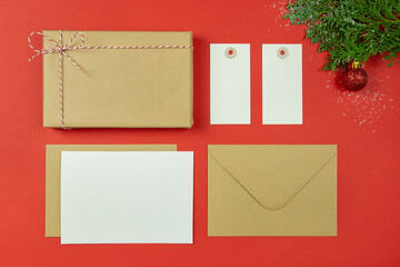 Christmas letter concept. Blank paper card, craft paper envelope, label, vintage gift box, rope, thuja branches on red background.Holiday Flat lay. Top view. Copy space. Mockup.