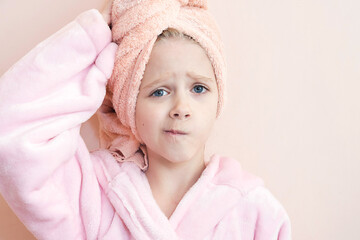 a little girl with blue eyes in a pink robe and a pink towel on her head after a bath smiles and looks into the frame. on a peach background