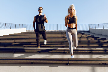 We work on the stairs. Sportive young couple in sportswear running together on stairs, outdoors
