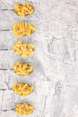 Italian foods concept and menu design. Various kind of Pasta Farfalle, Pasta A Riso, Orecchiette Pugliesi, Gnocco Sardo and Farfalle in spoons setup on white stone background