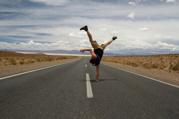 Young caucasian man breakdance move. Handstand in the asphalt desert road.