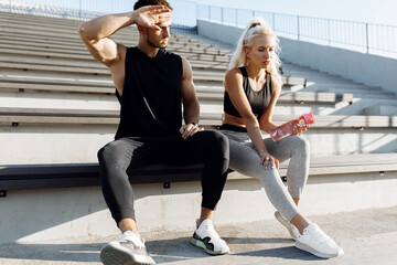 Young sportive couple in sportswear, taking a break to drink water, sitting on the stairs outdoors, healthy lifestyle