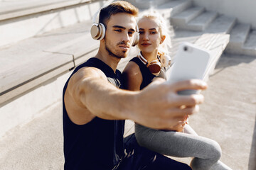 Sportive young couple, sitting on the stairs outdoors and taking a selfie on a mobile phone, fitness people after a successful workout