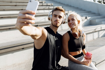 Sportive young couple, sitting on the stairs outdoors and taking a selfie on a mobile phone, fitness people after a successful workout