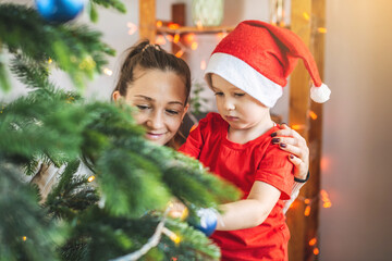 Mother with her child son is decorating the Christmas tree with toys and Christmas balls. Happy loving family on new year's eve