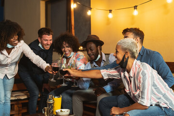Happy multiracial friends having fun during holidays toasting with cocktails and red wine on patio...