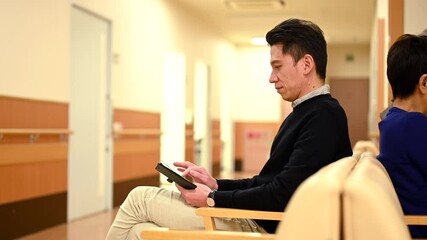 病院の待合室でスマートフォンの操作をする男性 - Powered by Adobe