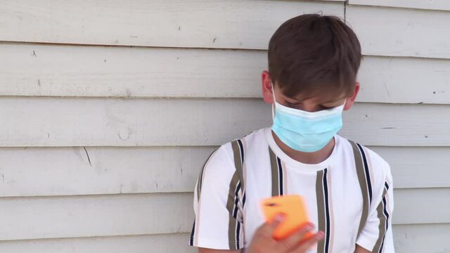 Teenage boy wearing face mask outside during Coronavirus COVID-19 Pandemic using mobile cell phone for social media