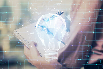Obraz premium Bulb hologram over hands taking notes background. Concept of idea. Double exposure