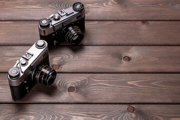 two vintage cameras stand against a background of brown wooden planks with space for copying
